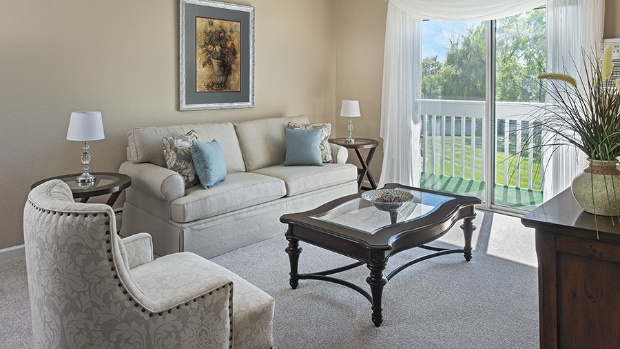 Apartment living room with balcony at American House independent living in South Sterling Heights, Michigan