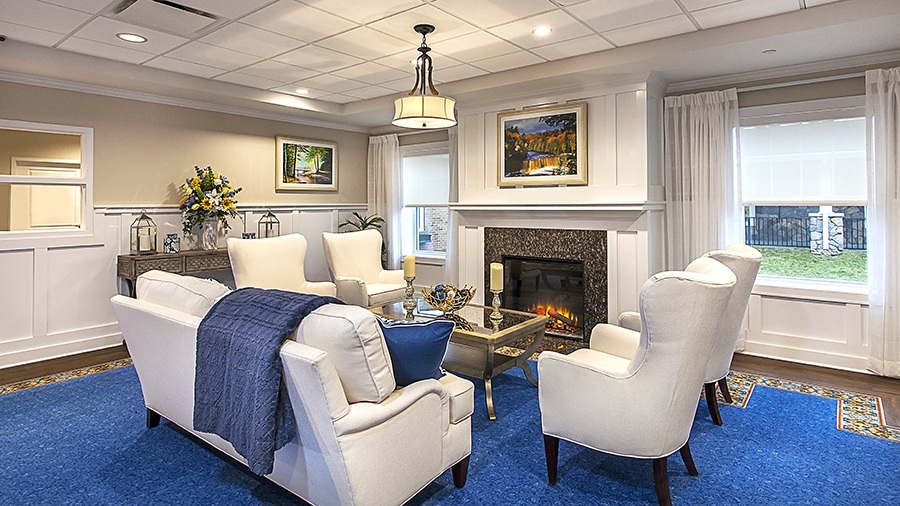 Comfy chairs and fireplace for gathering in memory care at American House Lakeshore senior living and memory care facility in Roseville, MI