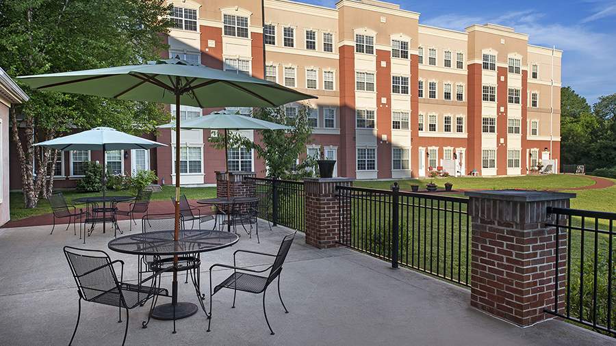 Tables with umbrellas on patio at American House Keene senior living community in Keene, NH
