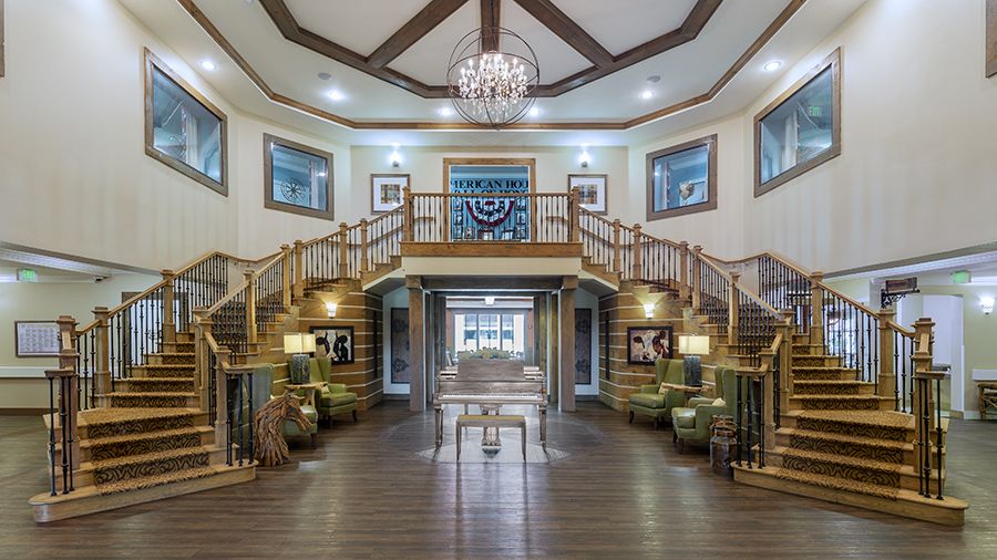 Main entryway with dual staircase and walnut colored piano in Wildwood senior living community.