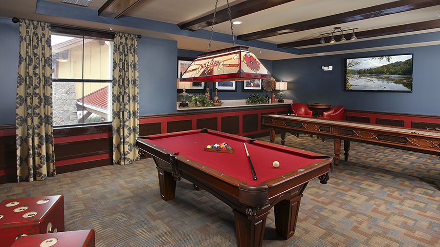 A game room with a red billiard table and a shuffle board table at American House Wildwood senior living communitye.