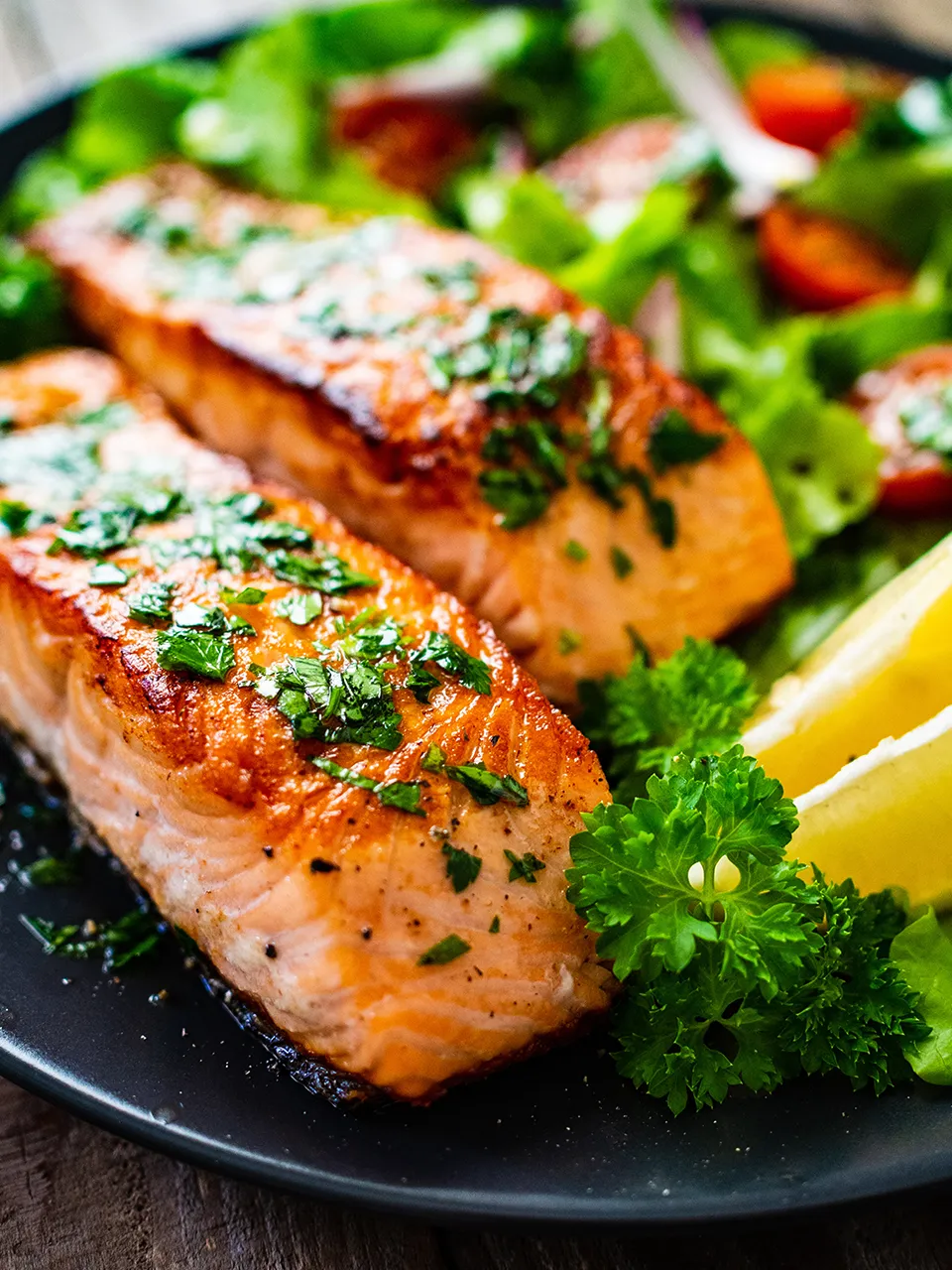 A salmon and pasta dish and a club sandwich with tomatoes and a pickle